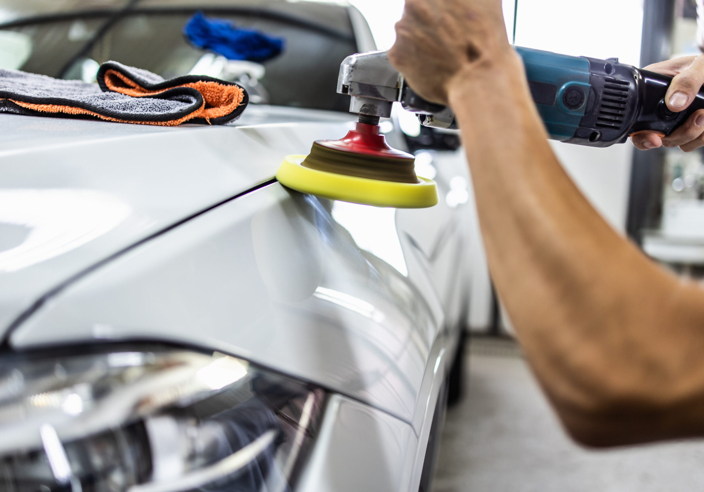 Car detailing - Hands with orbital polisher in auto repair shop. Close up shot. Selective focus.