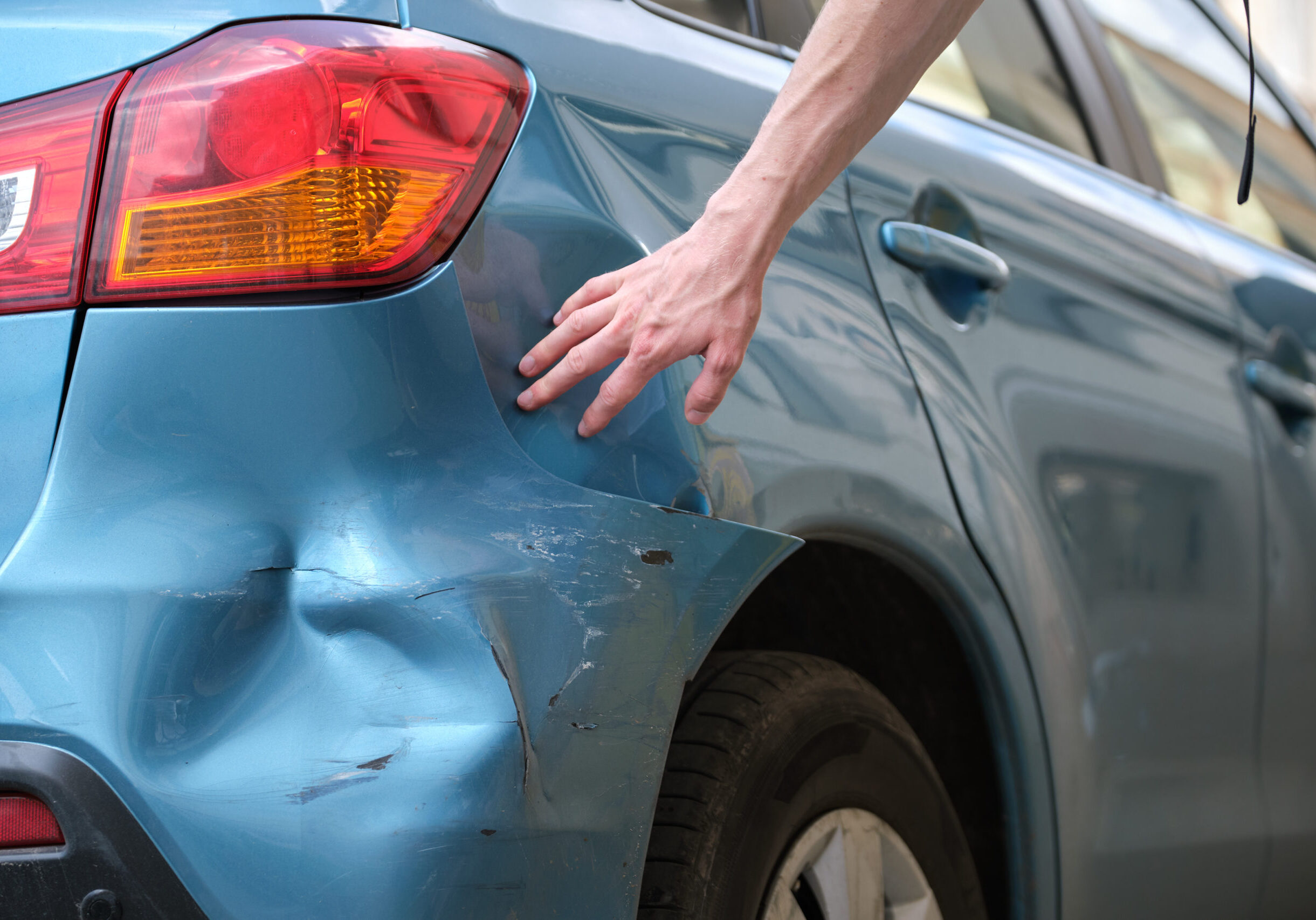 Driver hand examining dented car with damaged bumper